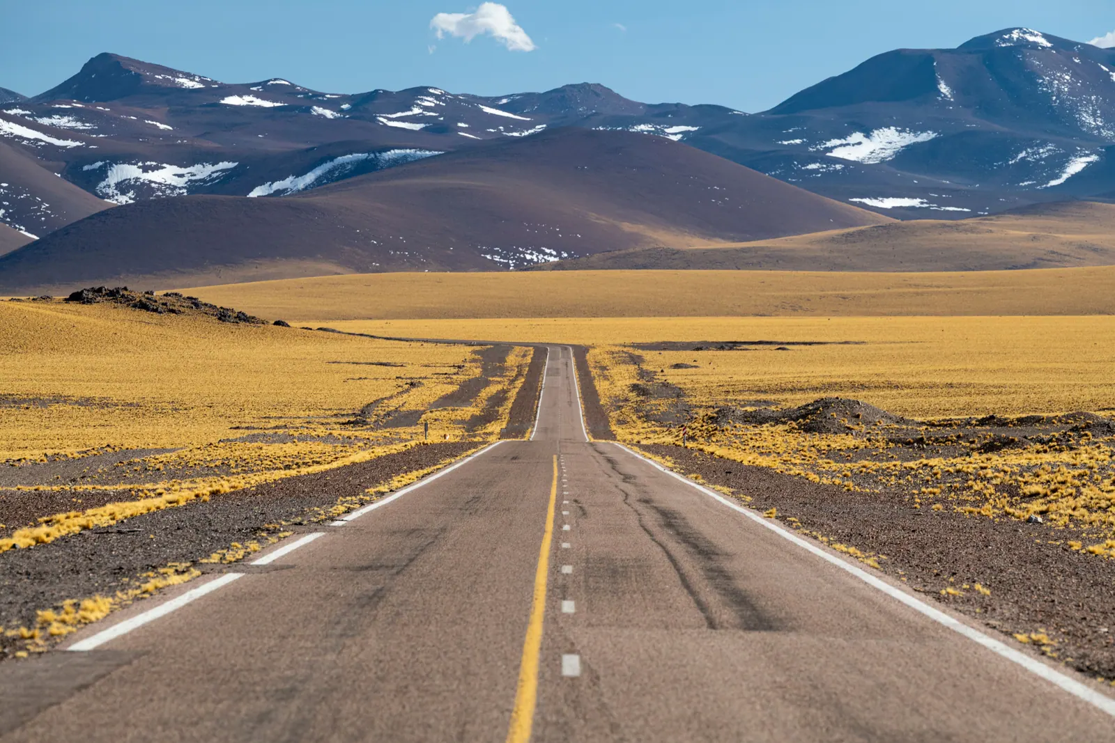 A long road crossing a desert landscape with mountains in the distance